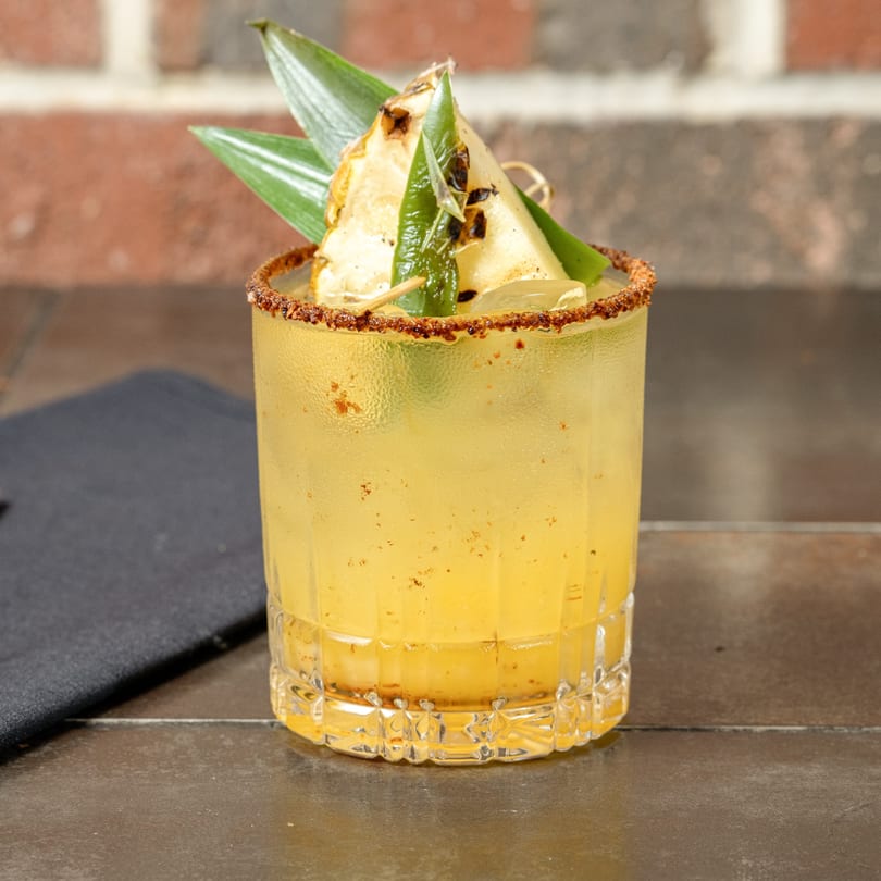 Havana 151's yellow cocktail with a spiced rim, garnished with grilled pineapple and green leaves.