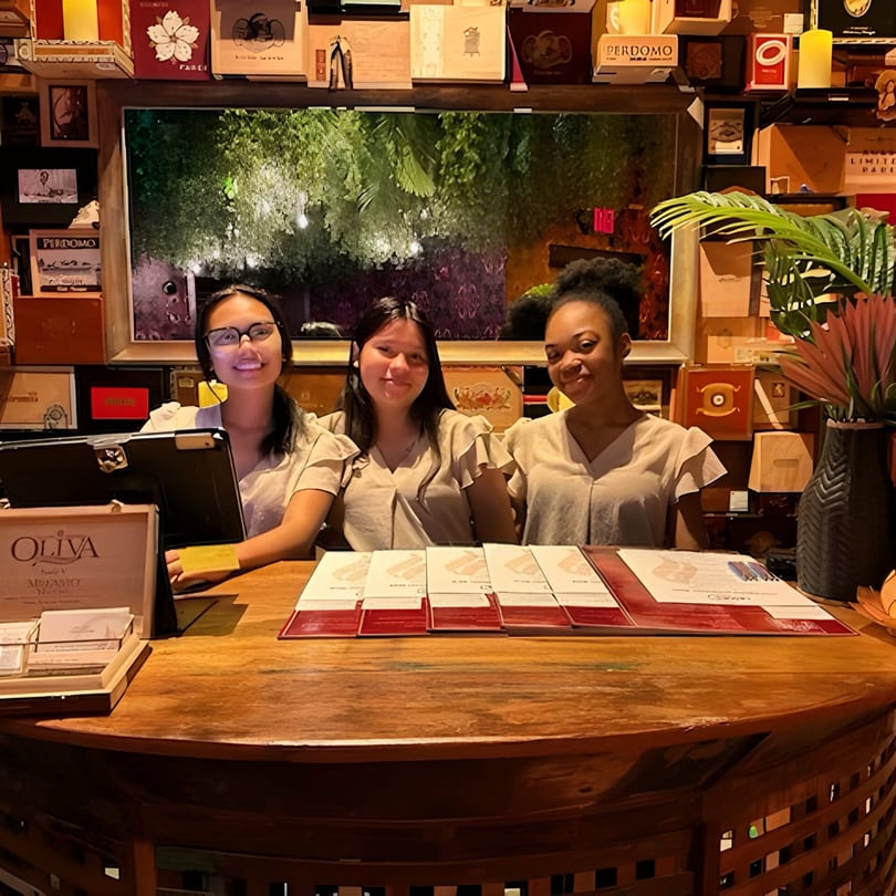 Three Havana 151 staff members smiling behind a wooden reception desk with menus and decor.
