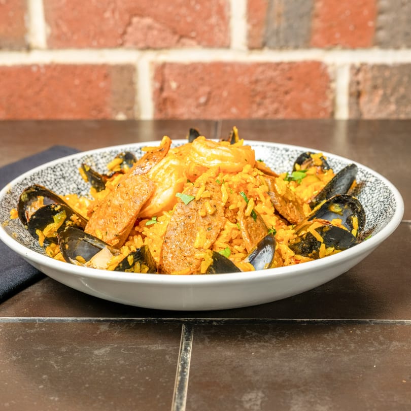 Cuban paella with yellow rice, mussels, shrimp, and sausage in a white bowl.