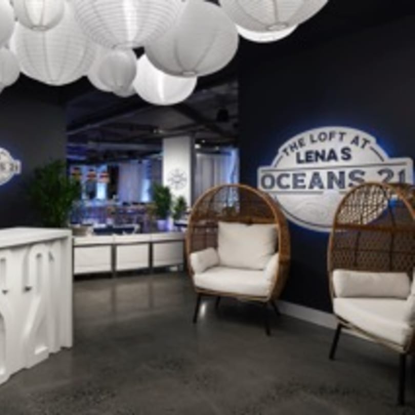 Lobby area with white paper lanterns, two wicker chairs, and a sign for "The Loft at Lena's Oceans 21".