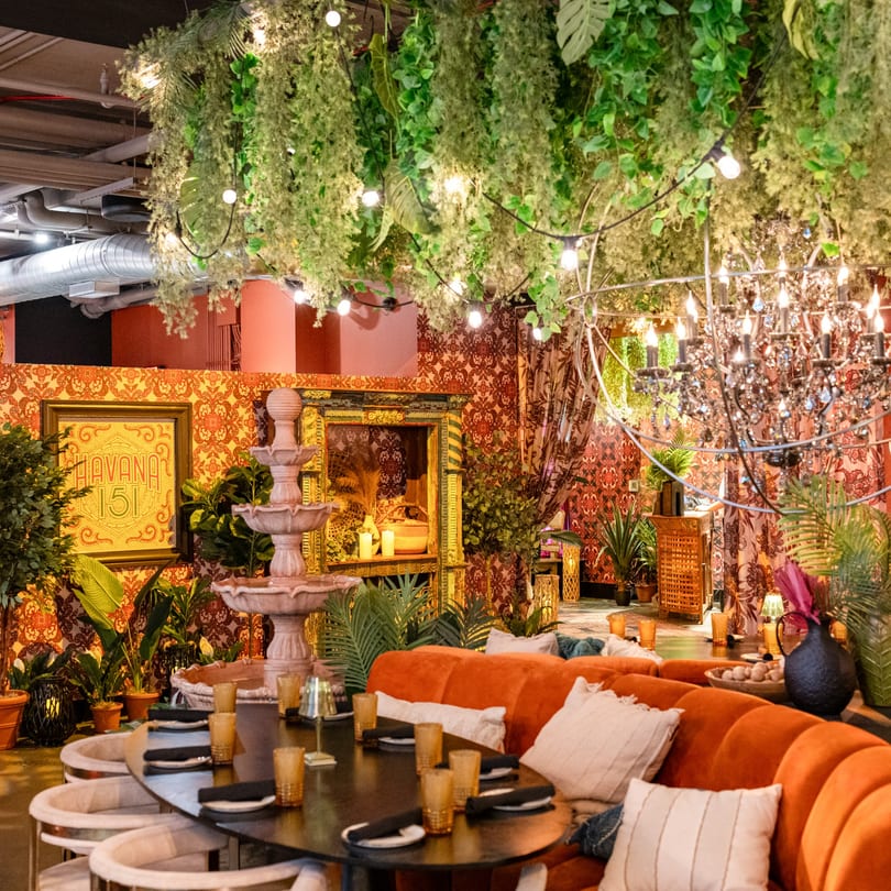 Havana 151 restaurant interior with lush greenery, patterned walls, a fountain, and orange seating.
