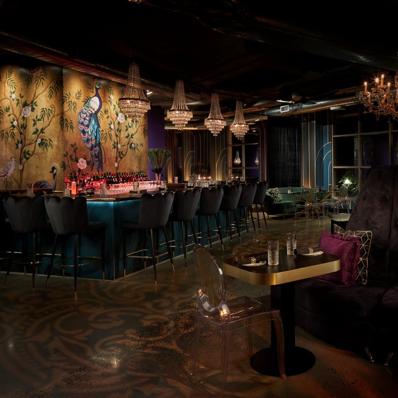 The Loft at Lena's bar with a peacock mural, chandeliers, and elegant seating.
