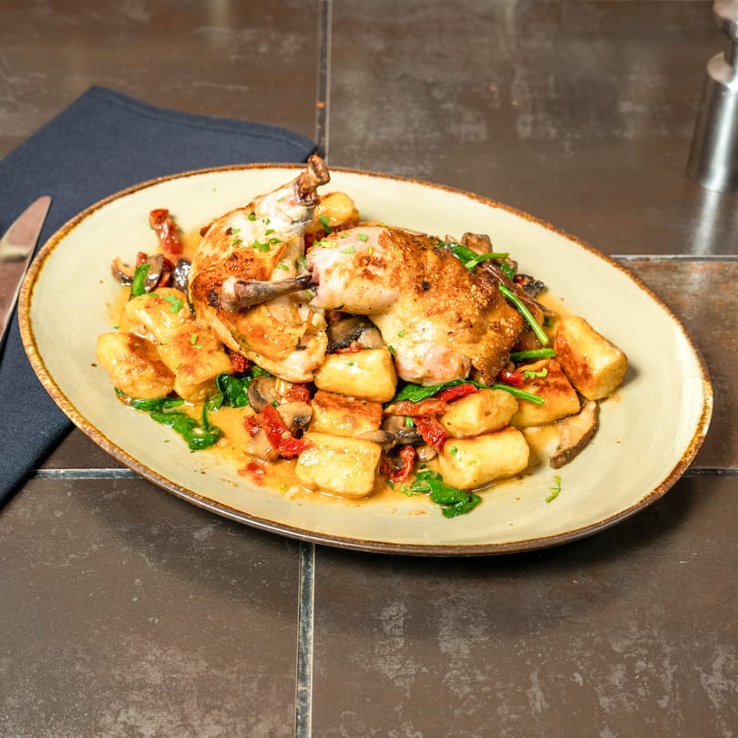 Havana 151's roasted chicken with gnocchi, spinach, mushrooms, and sun-dried tomatoes on an oval plate.