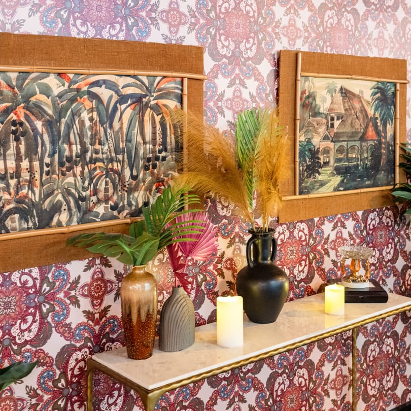 A console table with vases, candles, and framed artwork against a patterned wallpaper, evoking a Cuban atmosphere.