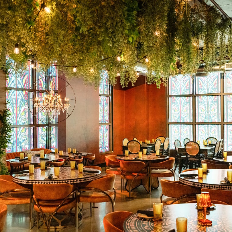 Havana 151's dining room with lush hanging greenery, ornate tables, and stained-glass windows.