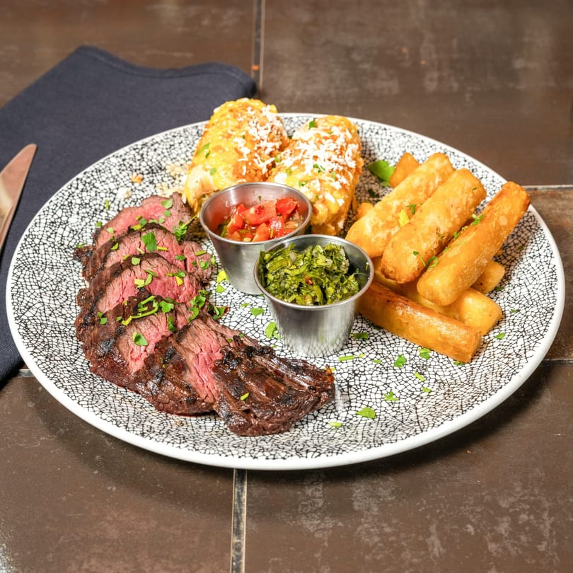 Havana 151's skirt steak with yuca fries, elote, and two dipping sauces on a patterned plate.