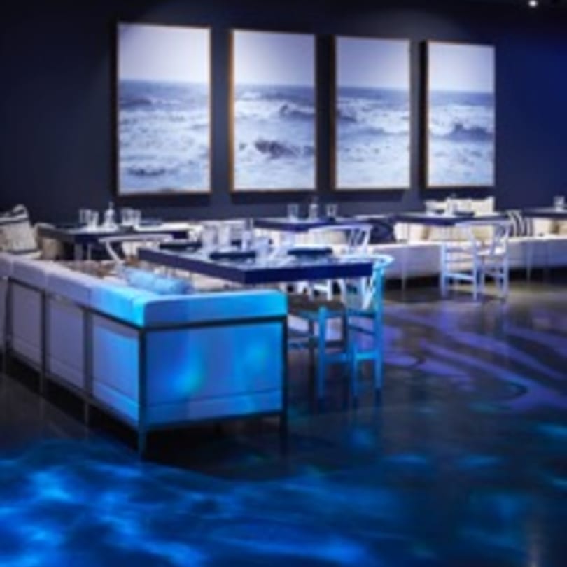 Havana 151's dining room with blue lighting, modern tables, white banquettes, and ocean artwork.