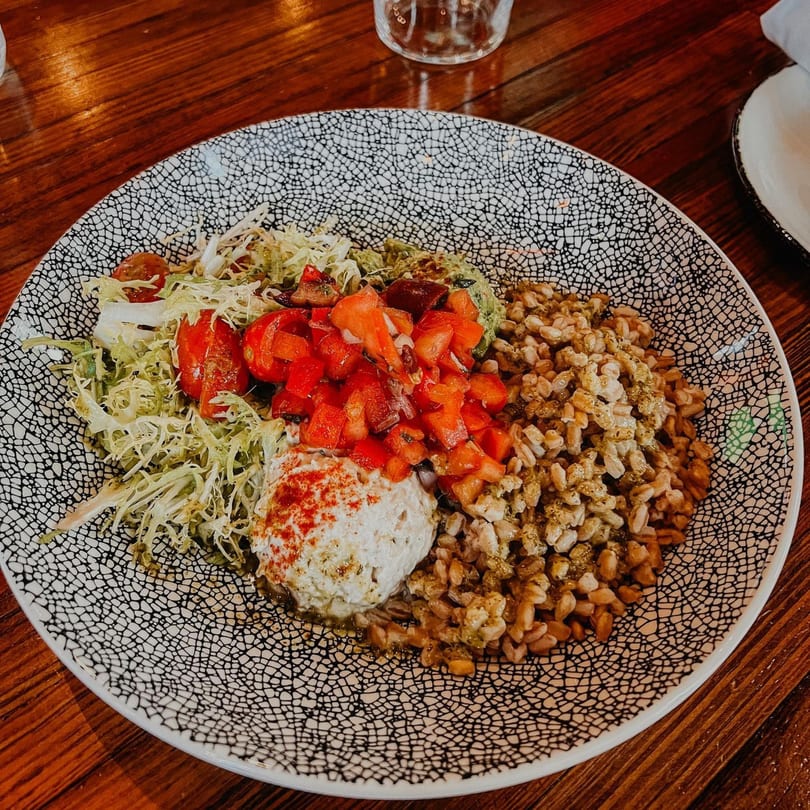 A Cuban bowl with rice, shredded lettuce, diced tomatoes, guacamole, and a dollop of white sauce.
