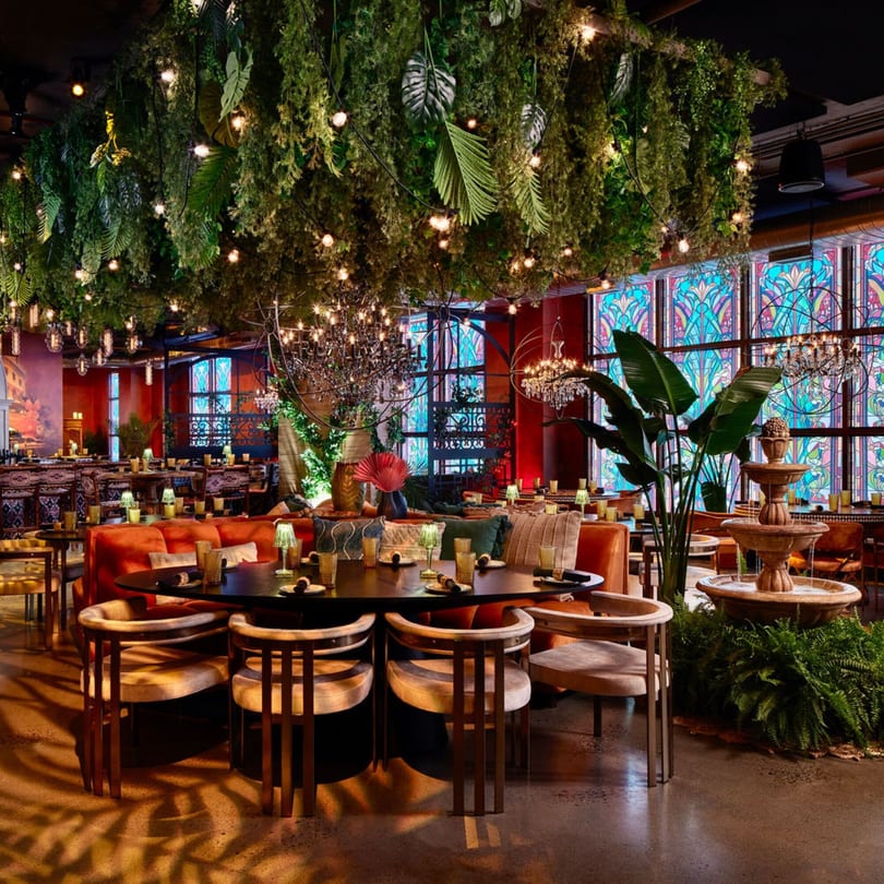 Havana 151 restaurant interior with lush hanging plants, ornate chandeliers, and stained-glass windows.