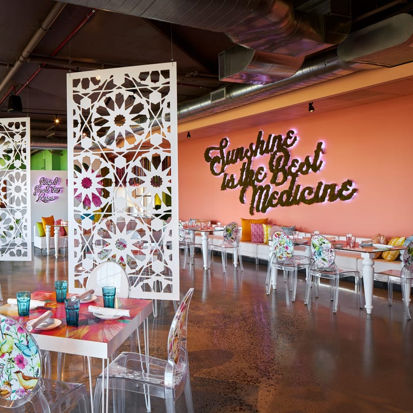 Vibrant Havana 151 dining room with coral walls, white lattice dividers, and clear chairs with floral backs.