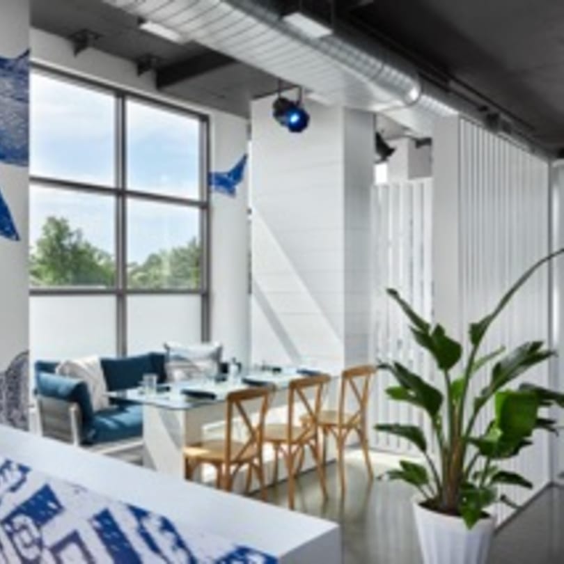 Bright, modern dining area at Havana 151 with large windows, blue seating, and wooden chairs.