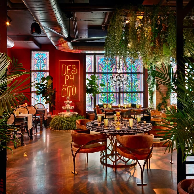 Havana 151's vibrant dining room with red walls, stained glass, lush plants, and a neon "DESPACITO" sign.
