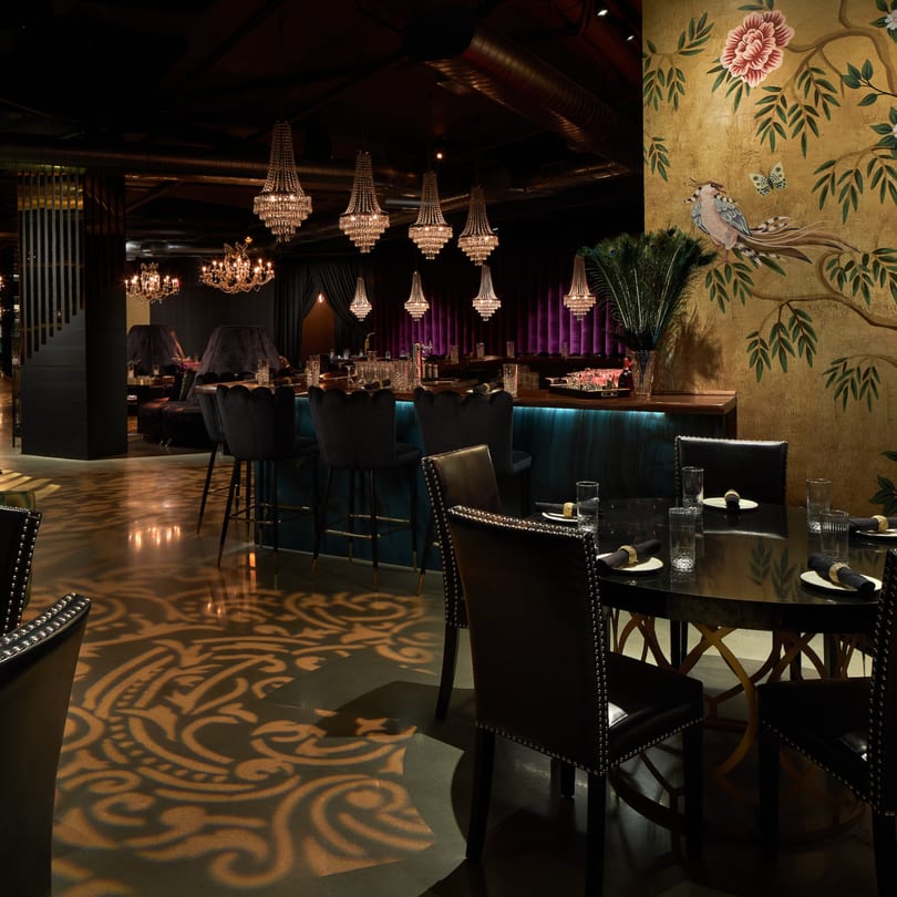 Dark, luxurious Havana 151 dining room with chandeliers, bar, and gold floral wall mural.