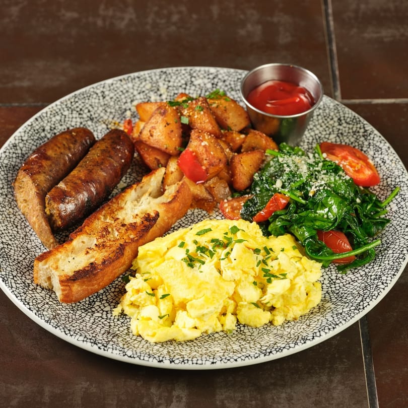 A Havana 151 breakfast plate with scrambled eggs, sausage, toast, home fries, and sautéed spinach.