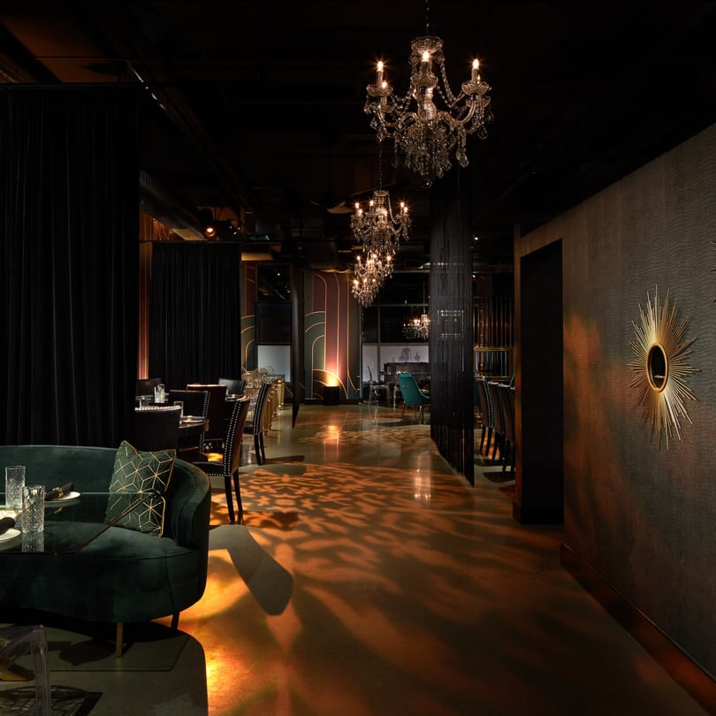 Elegant dining room at Havana 151 with chandeliers, dark velvet seating, and patterned lighting on the floor.