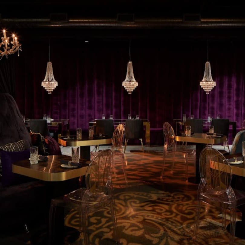 Elegant dining room at Havana 151 with purple velvet curtains, crystal chandeliers, and gold tables.