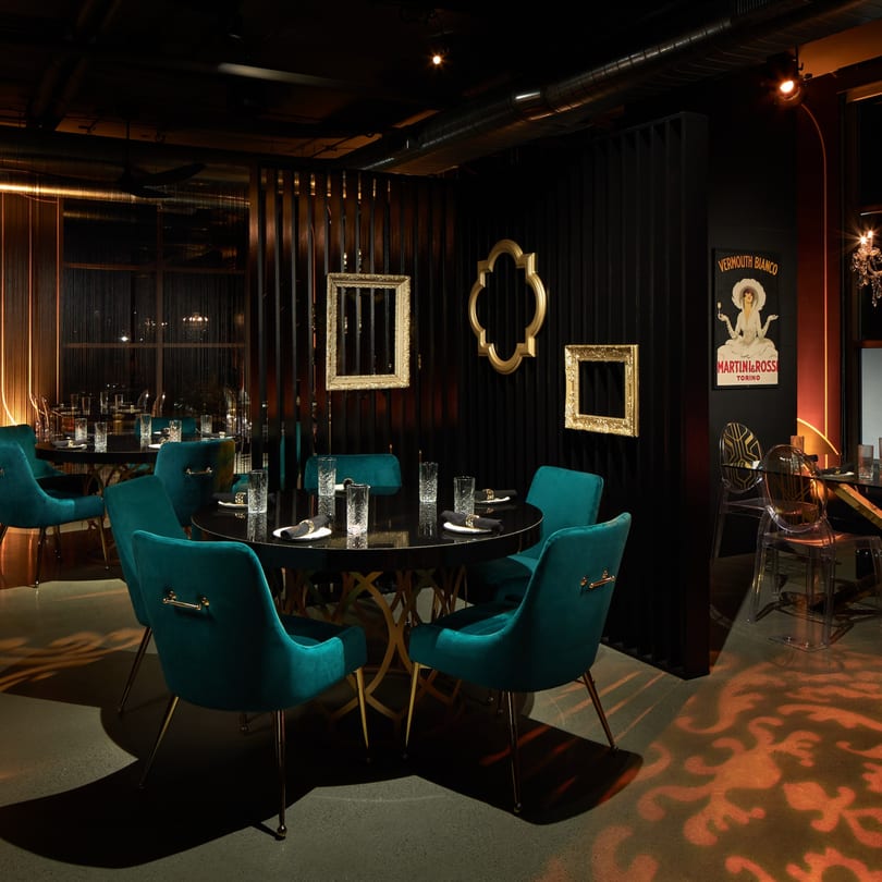 Havana 151's dimly lit dining area with teal velvet chairs, black tables, and gold accents.