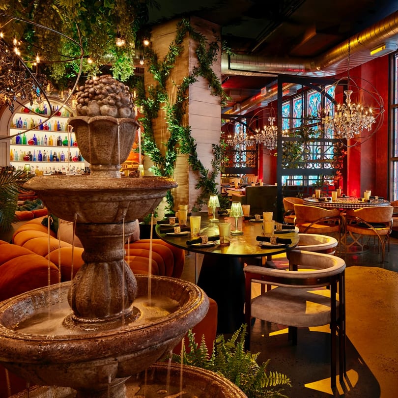 A Havana 151 restaurant interior with a fountain, lush greenery, chandeliers, and set tables.