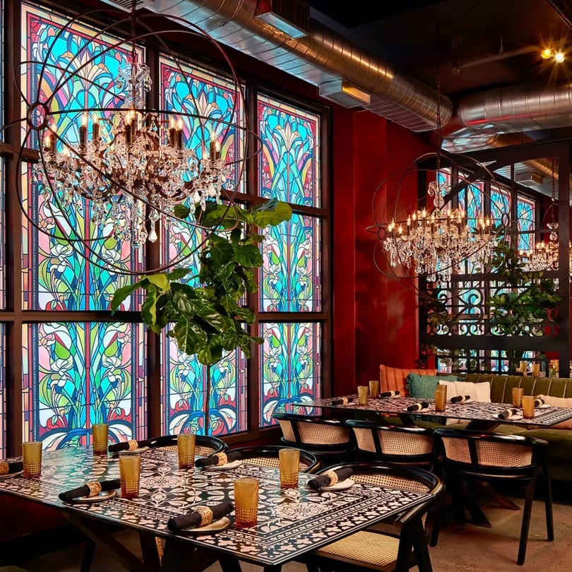 Havana 151's dining room features ornate chandeliers, stained glass windows, and patterned tables with wicker chairs.