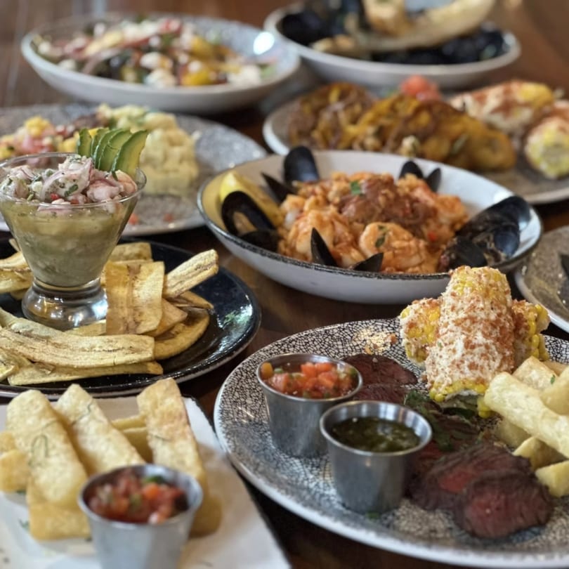 A table full of Cuban dishes, including ceviche, plantain chips, paella, and steak with corn.