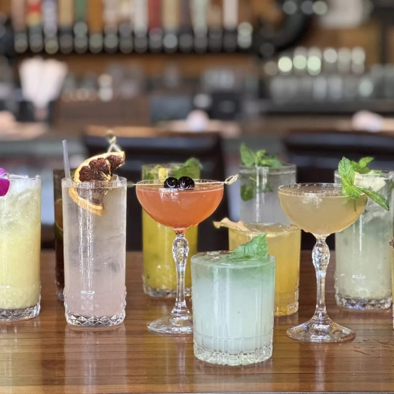 A variety of colorful Cuban cocktails with garnishes on a wooden bar top.